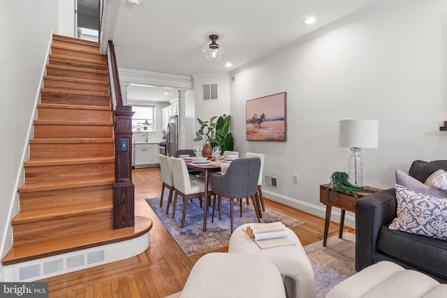 dining space with sink, light hardwood / wood-style flooring, ornamental molding, and decorative columns