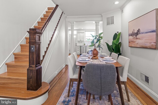 dining space featuring crown molding, wood-type flooring, and ornate columns