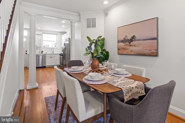 dining area with sink, ornamental molding, decorative columns, and light wood-type flooring