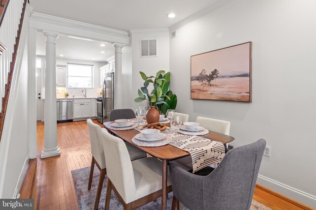 dining space with ornamental molding, sink, light hardwood / wood-style floors, and decorative columns