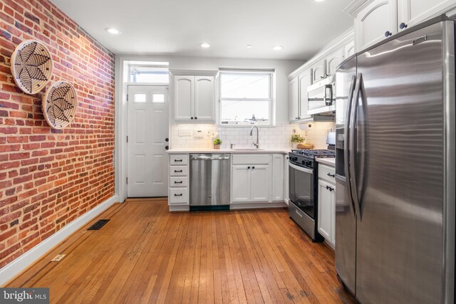 kitchen with sink, stainless steel appliances, white cabinets, and brick wall