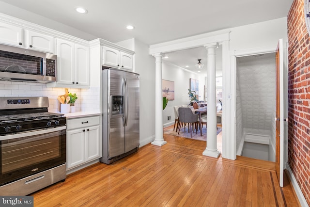 kitchen featuring ornate columns, appliances with stainless steel finishes, light hardwood / wood-style floors, and white cabinets