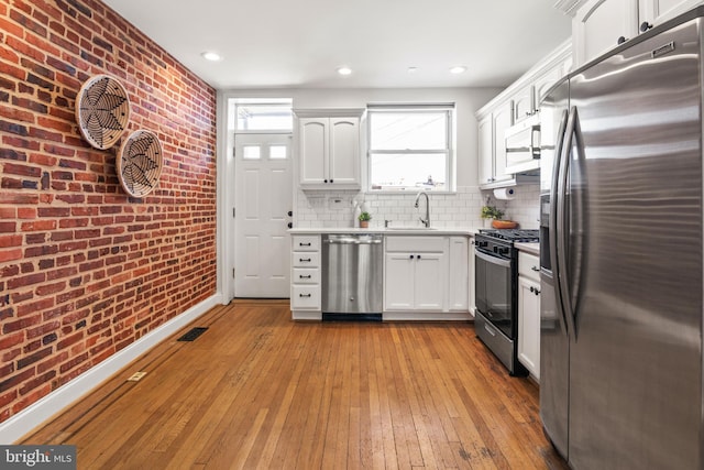 kitchen featuring brick wall, white cabinetry, and appliances with stainless steel finishes