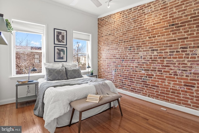 bedroom with brick wall, hardwood / wood-style floors, rail lighting, ornamental molding, and ceiling fan