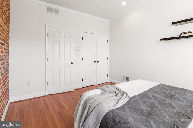 bedroom with light hardwood / wood-style flooring, ornamental molding, a closet, and brick wall