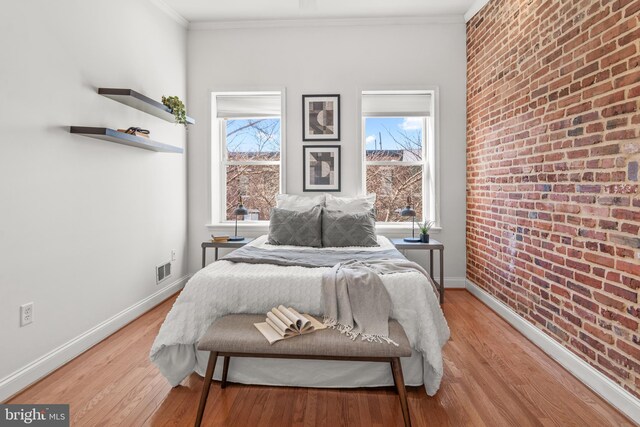 bedroom featuring ornamental molding, brick wall, and light hardwood / wood-style floors