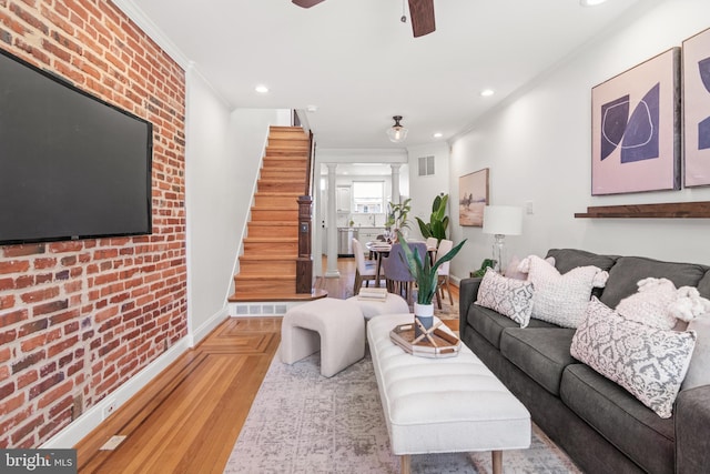 living room featuring ceiling fan, ornamental molding, and brick wall