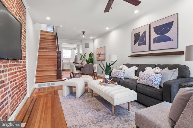 living room with hardwood / wood-style floors, crown molding, ceiling fan, and brick wall