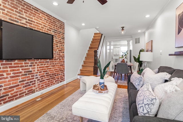 living room featuring wood-type flooring, ornamental molding, decorative columns, and brick wall