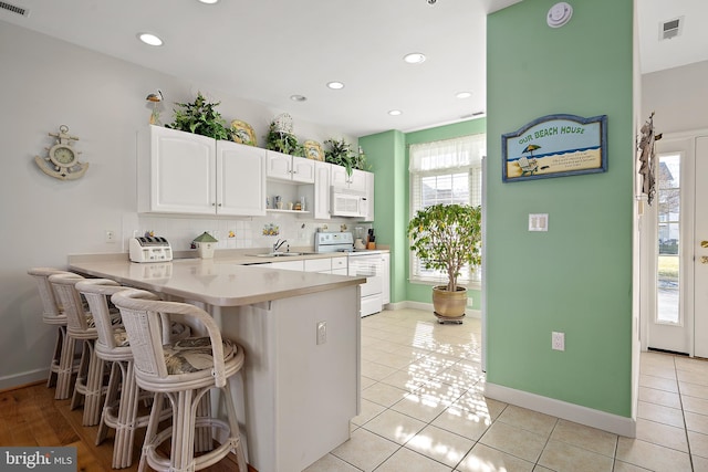 kitchen featuring white cabinetry, a kitchen bar, white appliances, and kitchen peninsula