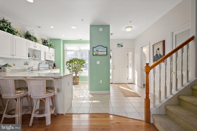 kitchen with white appliances, a breakfast bar area, white cabinetry, kitchen peninsula, and light wood-type flooring