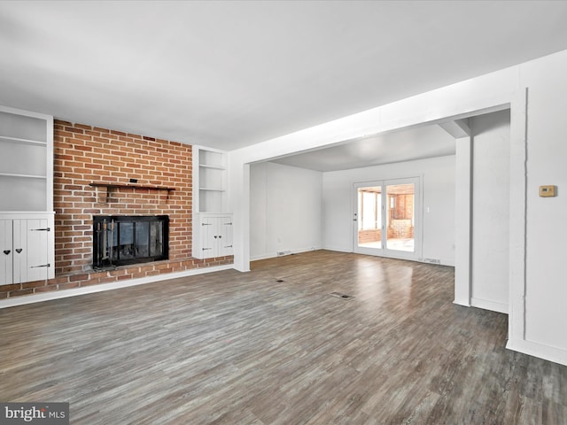 unfurnished living room featuring a brick fireplace, built in shelves, and dark wood-type flooring