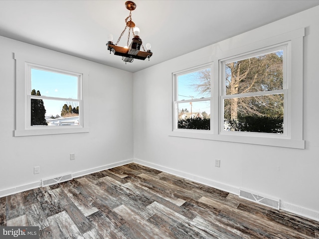 unfurnished room featuring dark wood-type flooring, a wealth of natural light, and a chandelier