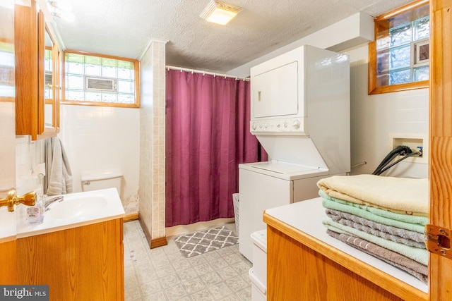 bathroom with stacked washer and dryer, a shower with shower curtain, vanity, a textured ceiling, and toilet