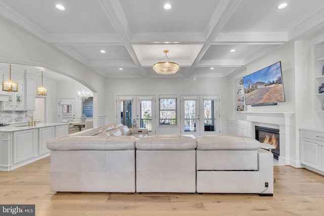 living room featuring coffered ceiling, light hardwood / wood-style floors, a chandelier, and beamed ceiling