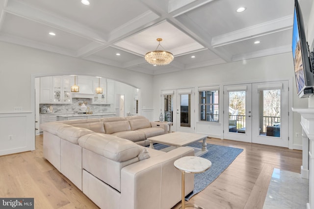 living room with coffered ceiling, an inviting chandelier, beam ceiling, and french doors