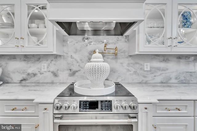 kitchen with premium range hood, light stone countertops, white cabinets, decorative backsplash, and stainless steel range with electric cooktop