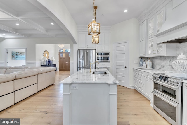 kitchen featuring decorative light fixtures, white cabinetry, stainless steel appliances, custom range hood, and a center island with sink