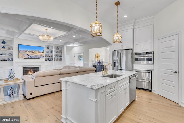 kitchen with appliances with stainless steel finishes, sink, white cabinets, hanging light fixtures, and a center island with sink