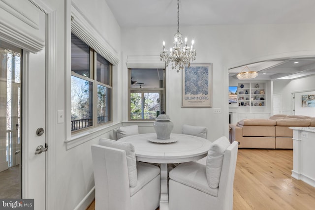 dining area with built in shelves, a notable chandelier, a fireplace, and light wood-type flooring