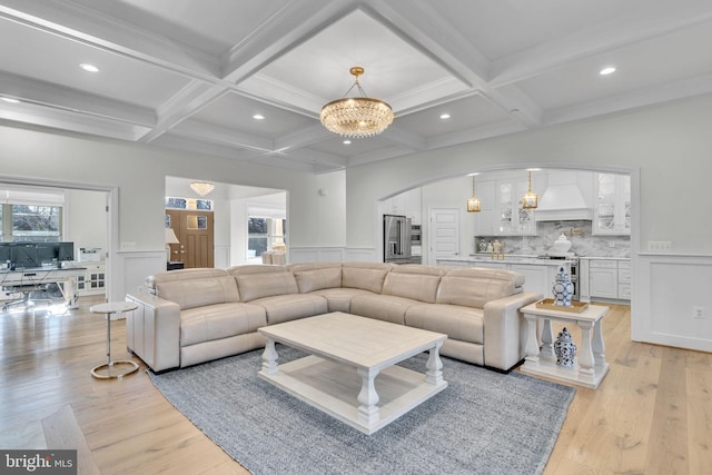 living room featuring an inviting chandelier, a healthy amount of sunlight, light hardwood / wood-style flooring, and beamed ceiling