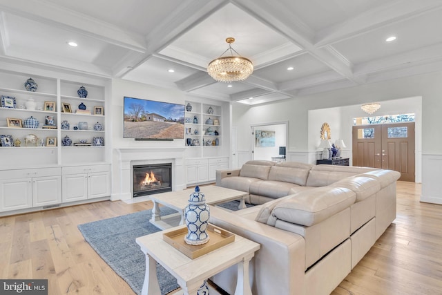 living room with beam ceiling, built in features, an inviting chandelier, and light hardwood / wood-style floors