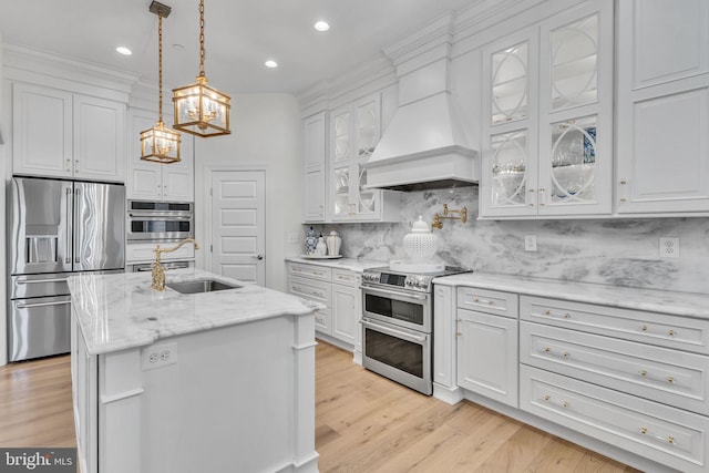 kitchen with pendant lighting, premium range hood, stainless steel appliances, an island with sink, and white cabinets