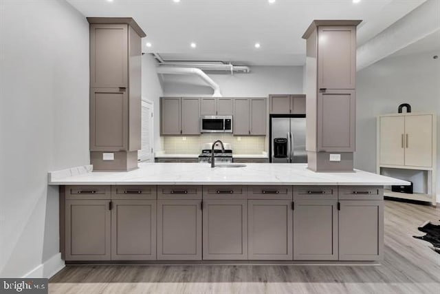 kitchen featuring tasteful backsplash, gray cabinets, kitchen peninsula, and appliances with stainless steel finishes