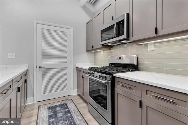 kitchen featuring gray cabinets, appliances with stainless steel finishes, backsplash, light stone counters, and light hardwood / wood-style floors