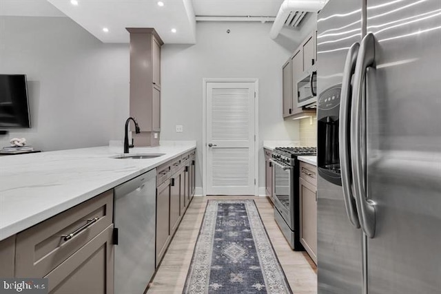 kitchen featuring sink, gray cabinets, light hardwood / wood-style flooring, appliances with stainless steel finishes, and light stone counters