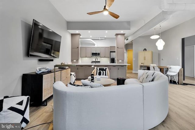 living room featuring sink, light hardwood / wood-style flooring, ceiling fan, and a high ceiling