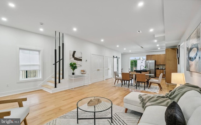 living room with a barn door, sink, and light hardwood / wood-style flooring