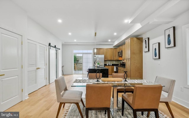 dining room with a barn door and light hardwood / wood-style flooring