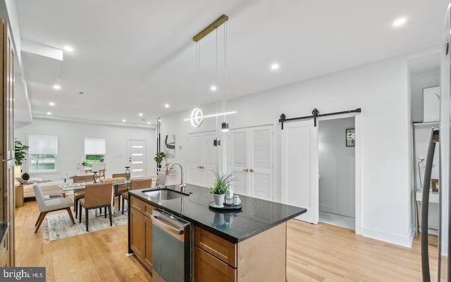 kitchen featuring pendant lighting, sink, stainless steel dishwasher, a barn door, and a center island with sink