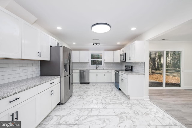 kitchen with white cabinetry, stainless steel appliances, sink, and light stone counters