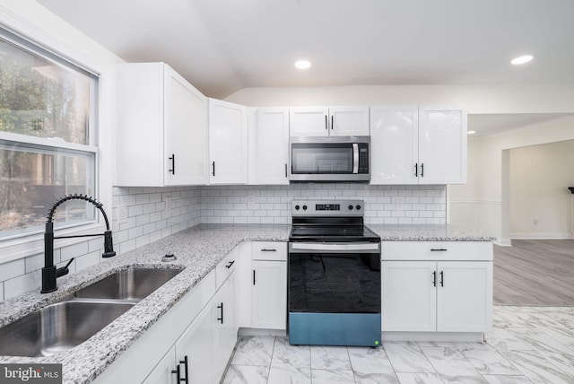 kitchen featuring stainless steel appliances, white cabinetry, light stone countertops, and sink