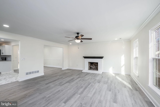 unfurnished living room with ceiling fan, ornamental molding, a brick fireplace, and light wood-type flooring