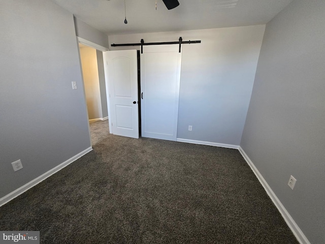 unfurnished bedroom with dark carpet, a barn door, and ceiling fan