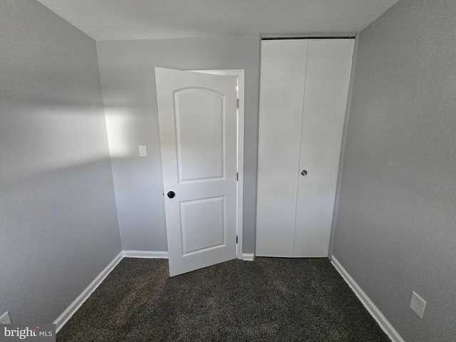 unfurnished bedroom with dark carpet and a closet