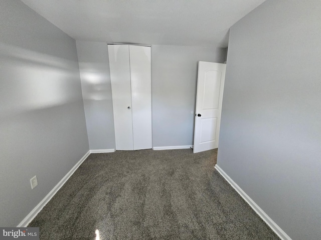 unfurnished bedroom with dark carpet and a closet