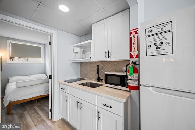 kitchen with tasteful backsplash, white cabinetry, sink, white fridge, and light hardwood / wood-style flooring