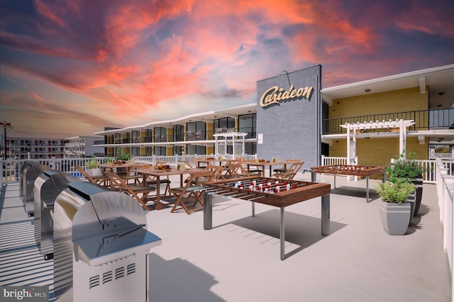 patio terrace at dusk with an outdoor kitchen, area for grilling, and a pergola