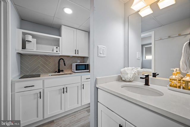 bathroom with wood-type flooring, vanity, a drop ceiling, and decorative backsplash