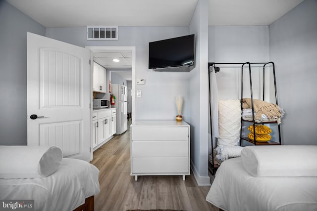 bedroom with light hardwood / wood-style floors and white fridge