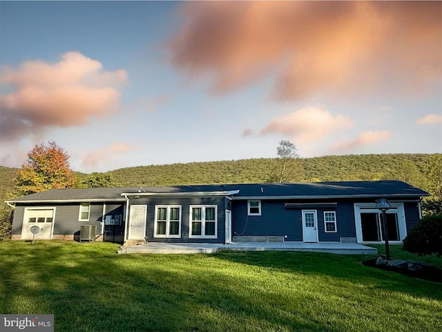 back house at dusk with central AC, a lawn, and a patio