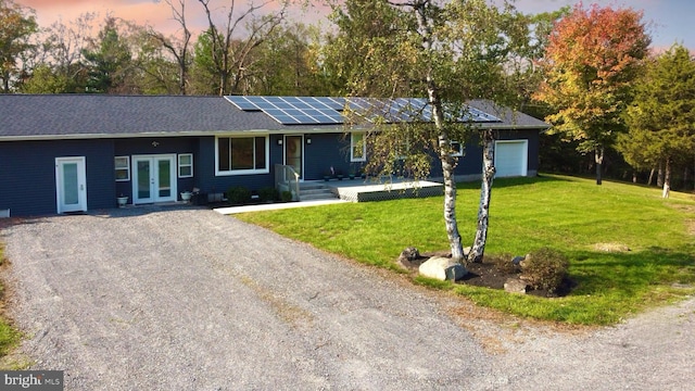 single story home with a garage, a lawn, french doors, and solar panels