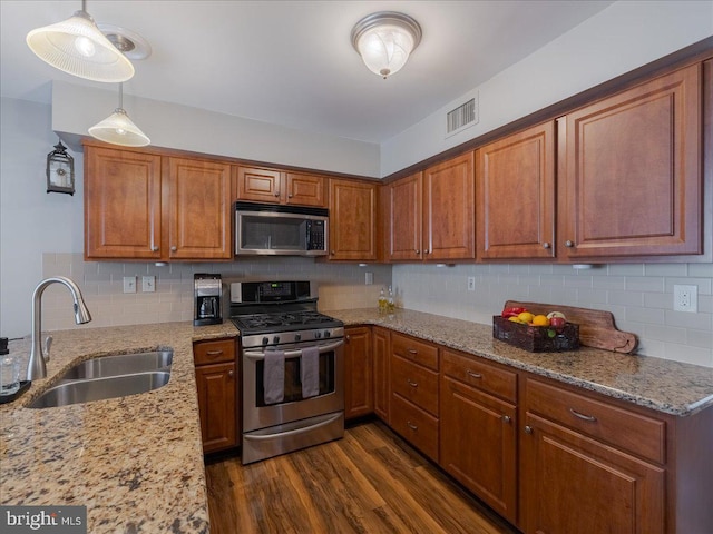 kitchen featuring appliances with stainless steel finishes, decorative light fixtures, sink, light stone countertops, and dark wood-type flooring