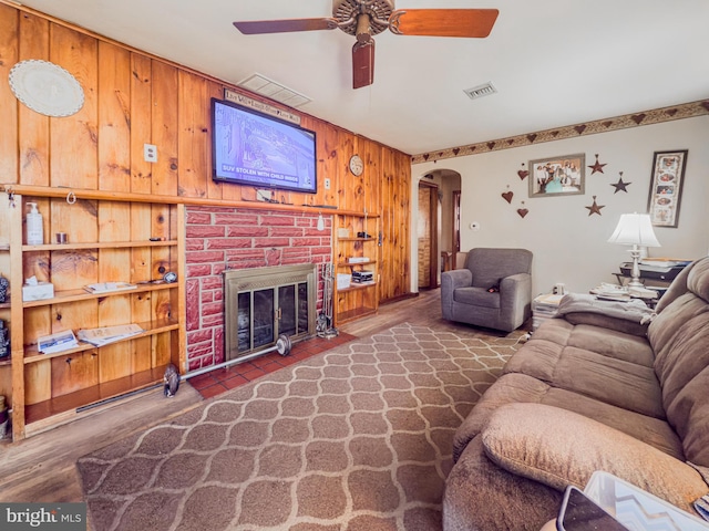 living room with ceiling fan, built in shelves, a fireplace, and wood walls