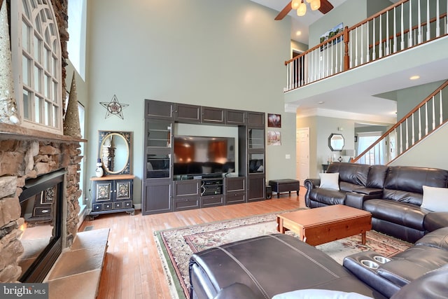 living room featuring a towering ceiling, a fireplace, ceiling fan, crown molding, and light wood-type flooring