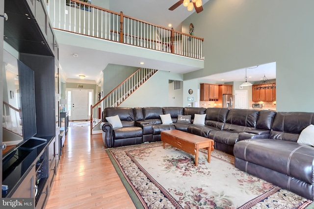 living room with ceiling fan, a towering ceiling, and light wood-type flooring